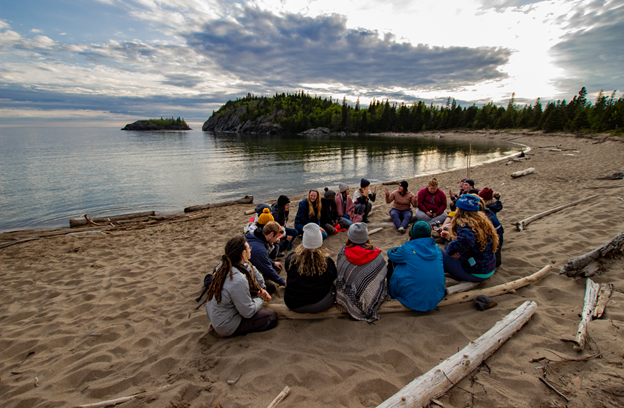 Ocean Bridge 2019 Great Lakes Cohort sit in a circle on a beach on Lake Superior